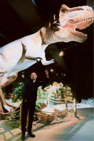 Cem Berk Senel below a life-size maquette of a Tyrannosorus Rex