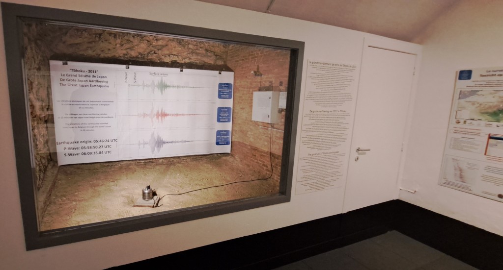 Une vitre derrière laquelle se trouve un séismomètre et un grand poster