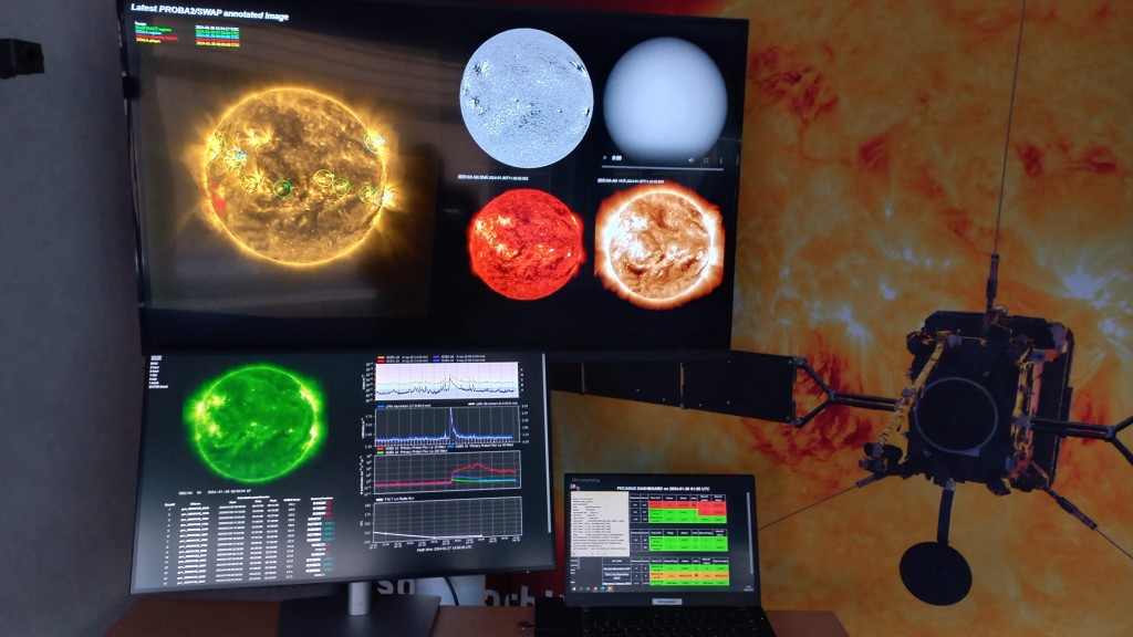 Screens with pictures of the sun behind which is an artist view of a satellite in front of the Sun