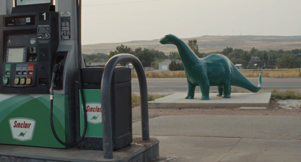 A dinosaur statue behind a Sinclair service station, which also has the same dinosaur as its logo.